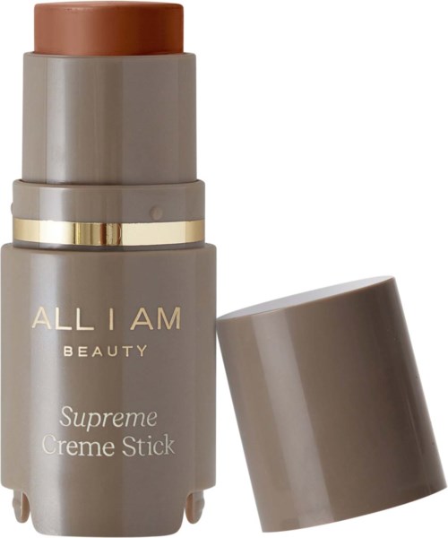 Eine graue zylindrische Verpackung mit goldener und weißer Beschriftung, bezeichnet als "ALL I AM BEAUTY Supreme Creme Stick," ohne Deckel.