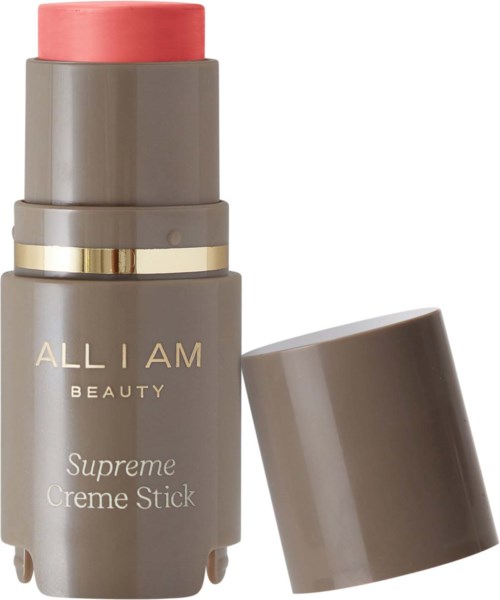 A beige and pink beauty stick with a gold band, labeled "ALL I AM BEAUTY Supreme Creme Stick," with the cap off.