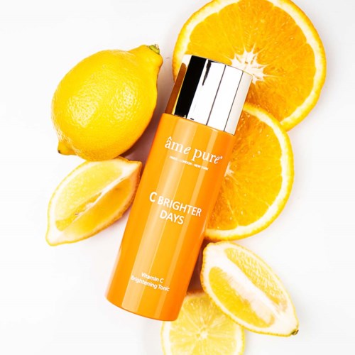 Eine leuchtend orangefarbene Hautpflegeflasche umgeben von Zitronenscheiben und einer ganzen Zitrone.