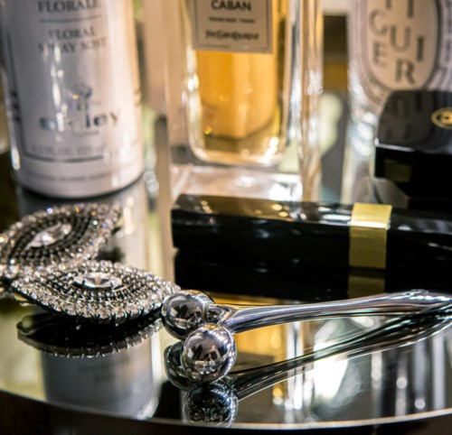 Eine Sammlung von Schönheits- und Schmuckartikeln, darunter Parfums, eine Halskette und ein Spiegel, auf einer glänzenden Oberfläche.