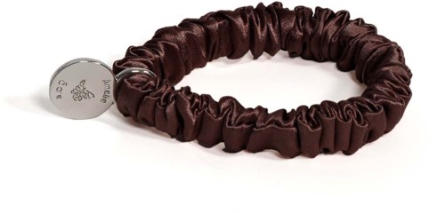 Ein braunes Satin-Haargummi mit kleinem silbernem Anhänger, auf einer weißen Oberfläche.
