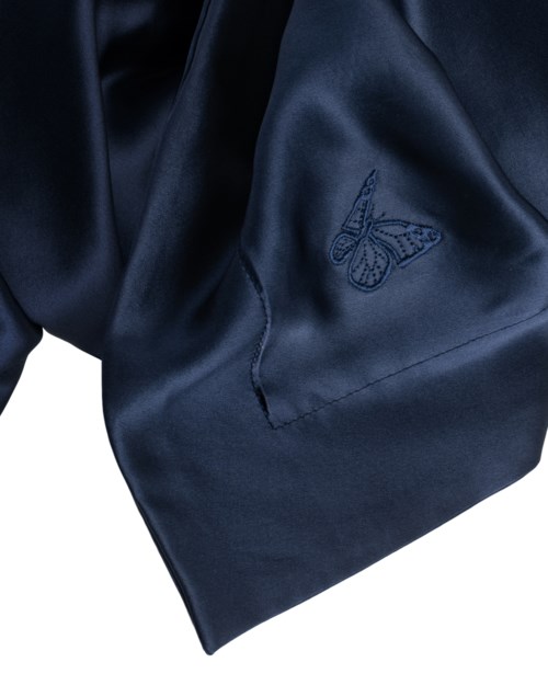 Dunkelblauer Stoff mit einem gestickten Schmetterlingslogo, sieht glatt und glänzend aus, möglicherweise Teil eines Kleidungsstücks.