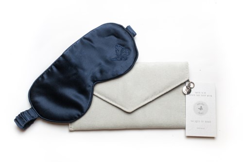 Eine dunkelblaue Schlafmaske, ein weißer Umschlag-Clutch und ein kleines Heft auf weißem Hintergrund.