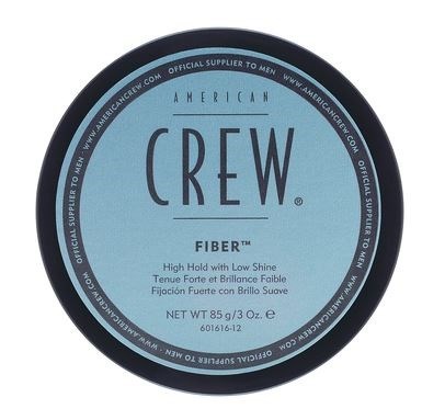 A circular label with a blue background, black border, and text about American Crew Fiber hair product.