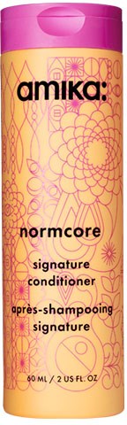 En rosa och gul flaska märkt 'Amika: Normcore Signature Conditioner' med blomm- och geometriska mönster.