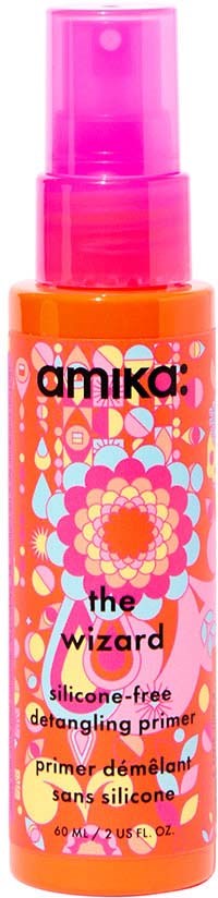 A bright orange bottle with a pink spray top features colorful floral and geometric designs. It is labeled "amika" and describes a silicone-free defrizzing primer.