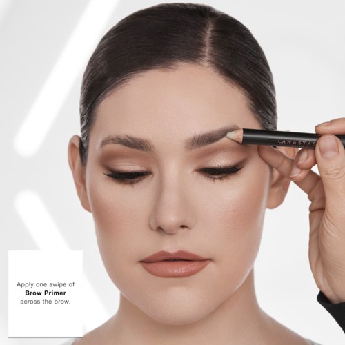 En kvinna med mörkt hår och naturlig makeup använder en ögonbrynprimer med en penna.