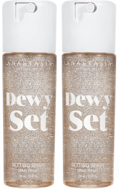 Zwei Flaschen Dewy Set Fixierspray mit beige Glitzer-Design und weißen Deckeln.