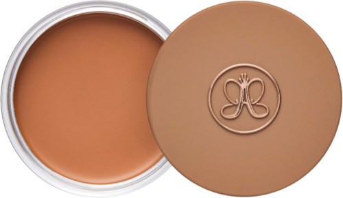 Ein runder Behälter mit hellbrauner Creme oder Foundation und einem passenden Deckel mit Logo.
