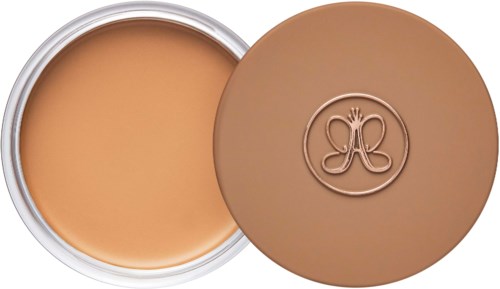 A round container with cream or foundation, and a lid with a logo of a butterfly inside a circle.
