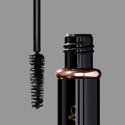 A black mascara tube with a brush applicator hanging beside it on a plain gray background.
