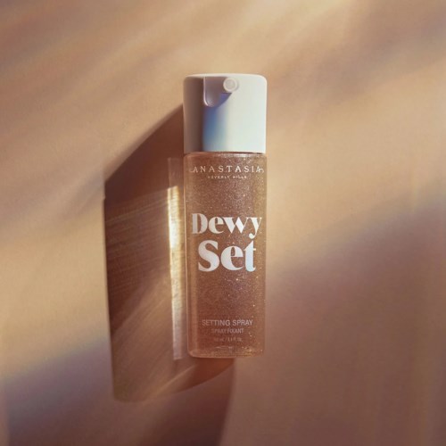 Ein Sprayflasche mit der Aufschrift 'Dewy Set' von Anastasia, mit einem hellen Deckel, auf beigem Hintergrund.