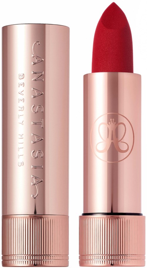 A red lipstick in a shiny pink case with a logo, standing upright next to its cap.