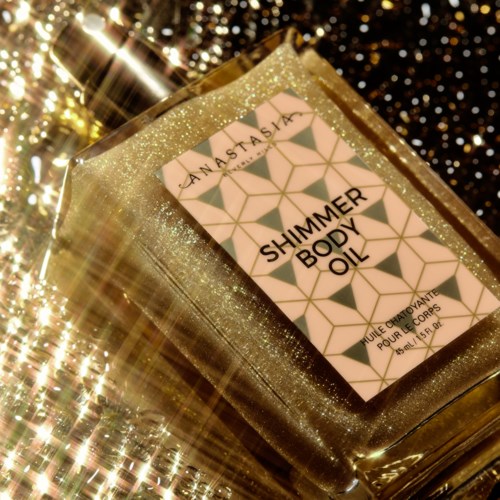 Een goudkleurige glitterdoos bevat een fles shimmer body oil op een glinsterend oppervlak.