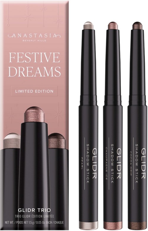 A set of three black makeup sticks with shimmery shades, placed in front of a pink box labeled Festive Dreams.