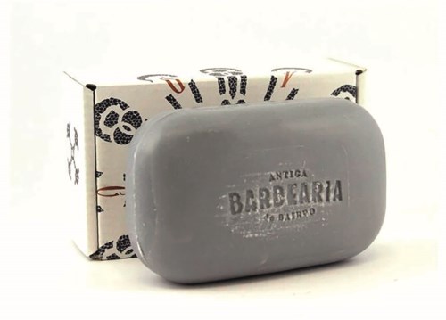 Ein grauer Seifenblock mit dem Text 'Antiga Barbearia' und einer Box mit Mustern im Hintergrund.