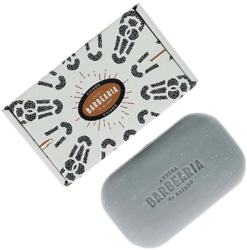Ein Seifenstück und eine Verpackung mit dem Logo 'Antiga Barbeira de Bano', graue Seife und gestalterisches Verpackungsdesign.