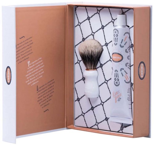 A shaving kit with a brush and cream, in a box with orange and white colors, and patterned paper inside.