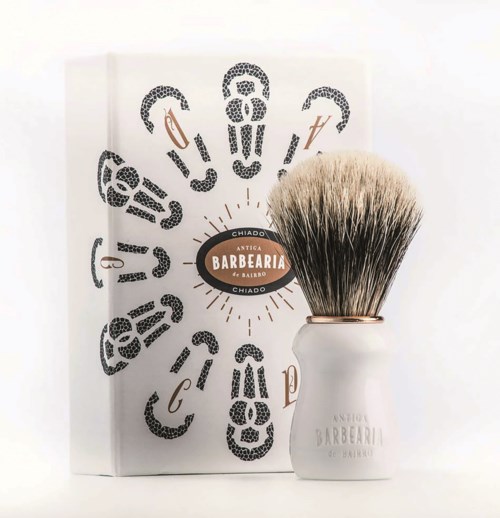 A shaving brush next to a box with a barber-themed design and text in Portuguese.