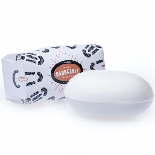 A white soap bar and its packaging with black and orange design elements. The package says "Barbearia".