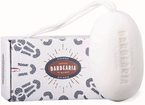 A white soap with a string handle in front of a box with pattern and text related to barbering.