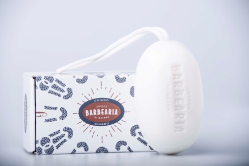 A white oval soap with a string, placed next to a box with blue patterns and text. The soap has some embossed letters.
