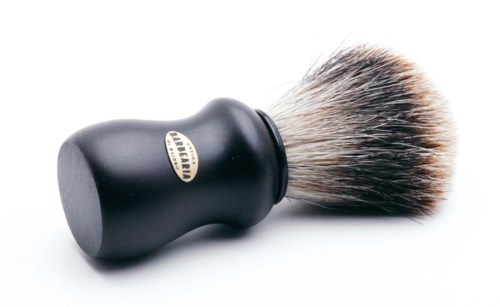 A shaving brush with black handle and soft bristles, placed on a white surface.