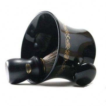A black coffee mug with gold decorations, lying on its side with a brush inside.