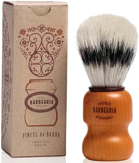 A shaving brush with a wooden handle and white bristles, next to its cardboard packaging with decorative design.