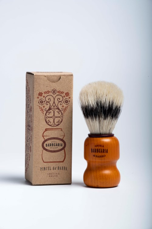 A shaving brush with a wooden handle and a cardboard box with decorative design and text.