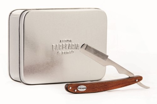 A silver shaving kit with a straight razor in front of it. The kit has text and a logo on its surface.