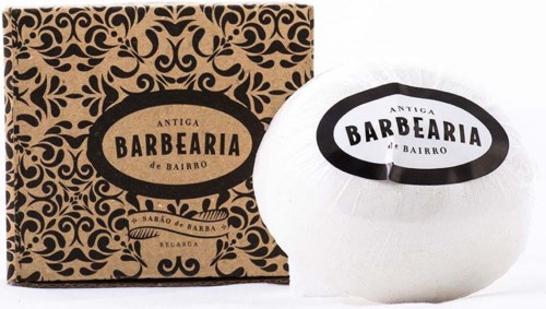 A white shaving soap in a round container next to a decorative brown and black box, both labeled 'Barbearia' and 'Antiga'.
