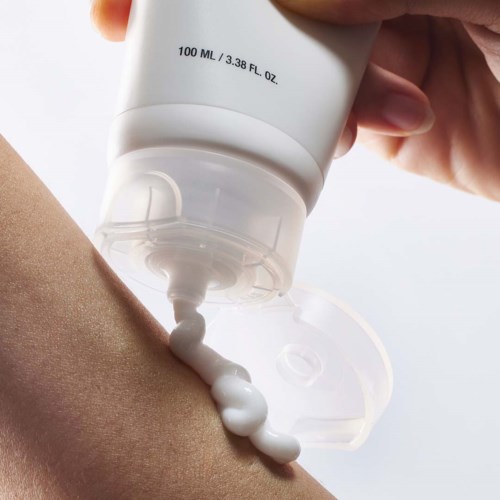 En hand trycker ut vit lotion från ett rör till armen. Rörmärket är 100 ML eller 3,38 FL OZ.