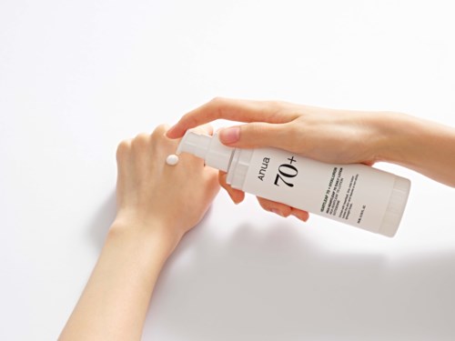 Iemand gebruikt zonnebrandcrème met SPF 70+ op hun hand. De fles is wit met zwarte en groene tekst.