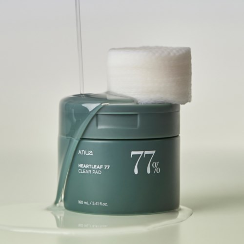 Een turkoois container met Anua Heartleaf 77 Clear Pads, een wattenschijfje bovenop en vloeistof die eruit loopt.