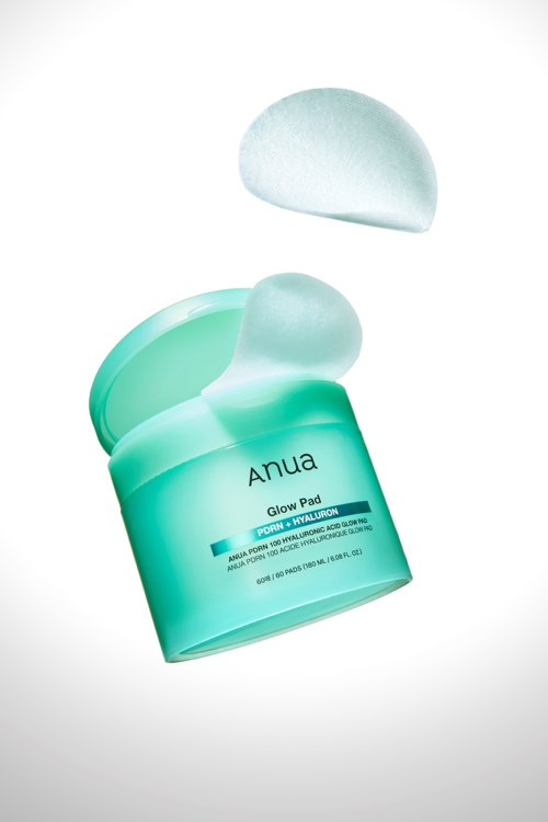 Groene container met deksel, gemerkt 'Anua Glow Pad', open met een wit wattenschijfje erboven.
