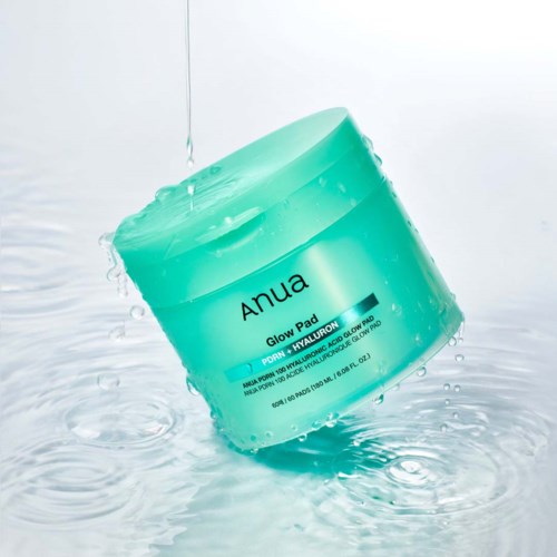 En turkis krukke med Anua Glow Pad hudpleieprodukt med vann som spruter rundt.
