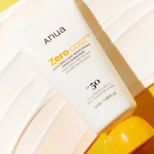 A white bottle of Anua Zero-Cast SPF 50 sunscreen with a yellow cap, leaning against a white wall.