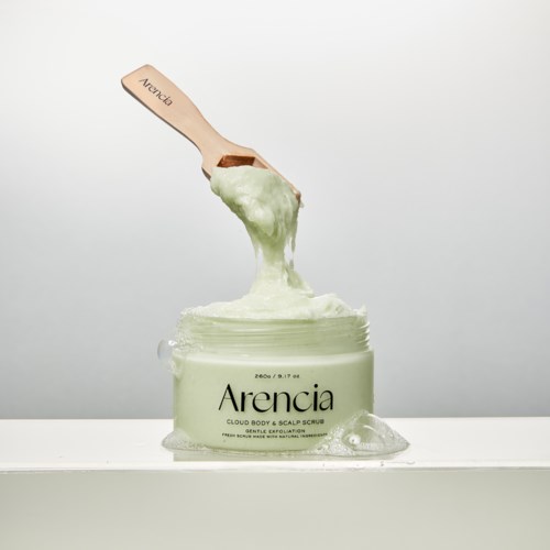 Ein Behälter mit Arencia Kopfhautpeeling, Holzschöpfkelle gießt hellgrünes Peeling aus. Sauberer Hintergrund.