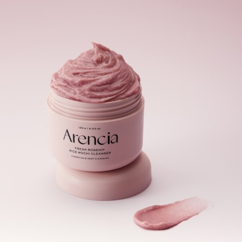 Ein rosa Becher mit Hautpflegecreme beschriftet Arencia Fresh Rosehip mit etwas Creme daneben.