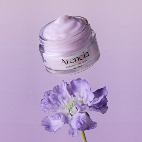 Ein Glas mit weißer Creme und eine lila Blume vor lila Hintergrund.