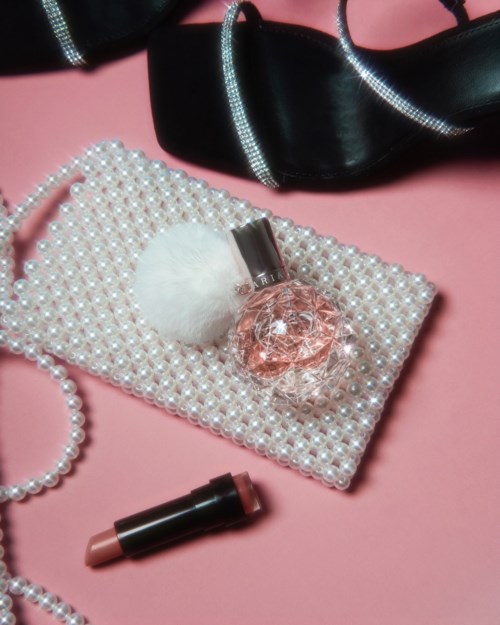 Sieraden, lippenstift en een parelmoer clutch op een roze achtergrond met een zwarte schoen in de buurt.