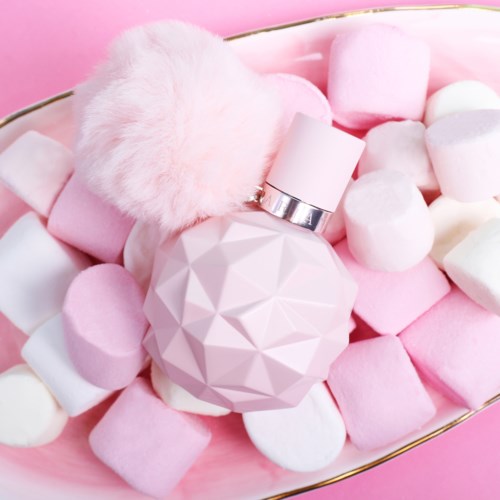 Roze geometrische parfumfles met een fluffy pom-pom, omringd door marshmallows op roze achtergrond.