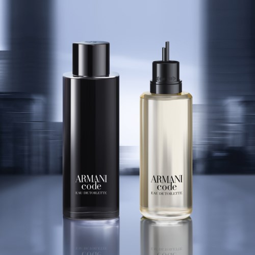 Två Armani Code parfymflaskor, en svart och en klar, på en reflekterande yta med en suddig bakgrund.