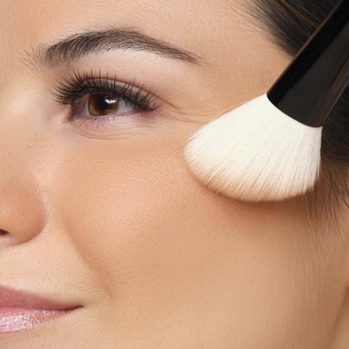 Een vrouw brengt make-up aan met een grote kwast op haar wang dicht bij haar oog.