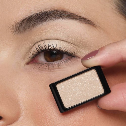 Närbild på en kvinna som applicerar skimrande highlighter på kinden med en liten makeup-penna.