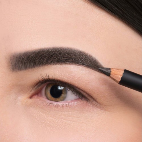 Eine Person füllt eine Augenbraue mit einem Stift oder Pinsel aus. Der Fokus liegt auf Auge und Augenbraue.