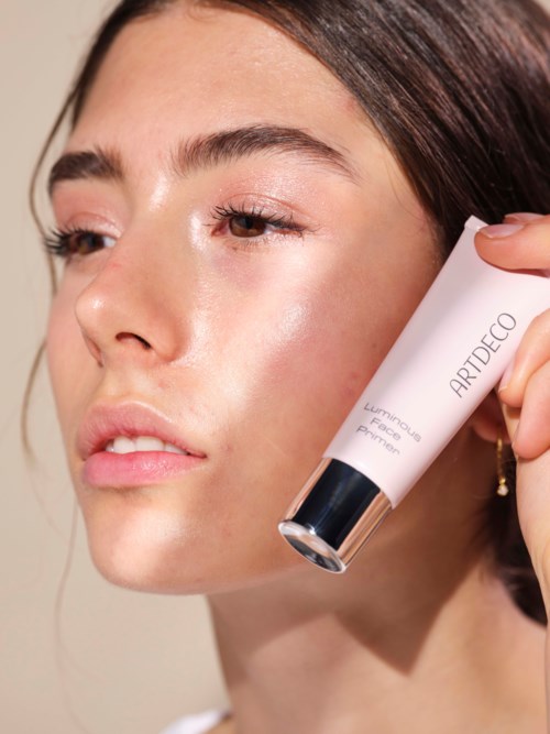 Een vrouw brengt een huidverzorgingsproduct aan op haar gezicht, houdt een tube met 'ARTDECO Luxury Face Primer'.