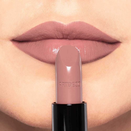 Nahaufnahme von Lippen mit Nude-Lipstick, der Lippenstift gegen die Lippen hält.