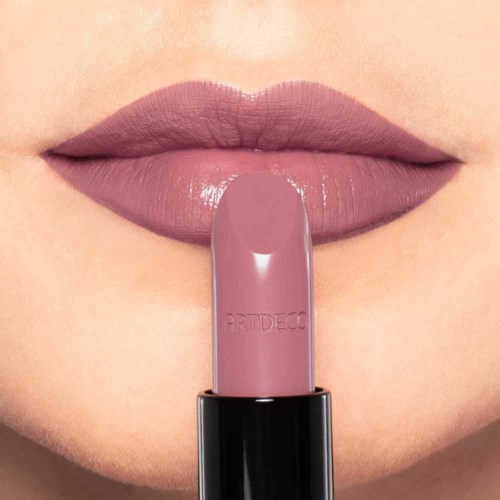 Die Lippen einer Person sind mit rosa Lippenstift gefärbt, und ein passender Lippenstift liegt vertikal auf den Lippen.